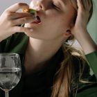 Portrait of a young woman savoring sushi with a wine glass in a relaxed, green-themed setting.