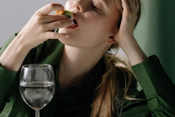 Portrait of a young woman savoring sushi with a wine glass in a relaxed, green-themed setting.