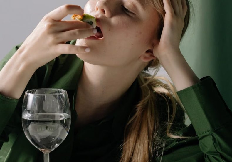 Portrait of a young woman savoring sushi with a wine glass in a relaxed, green-themed setting.